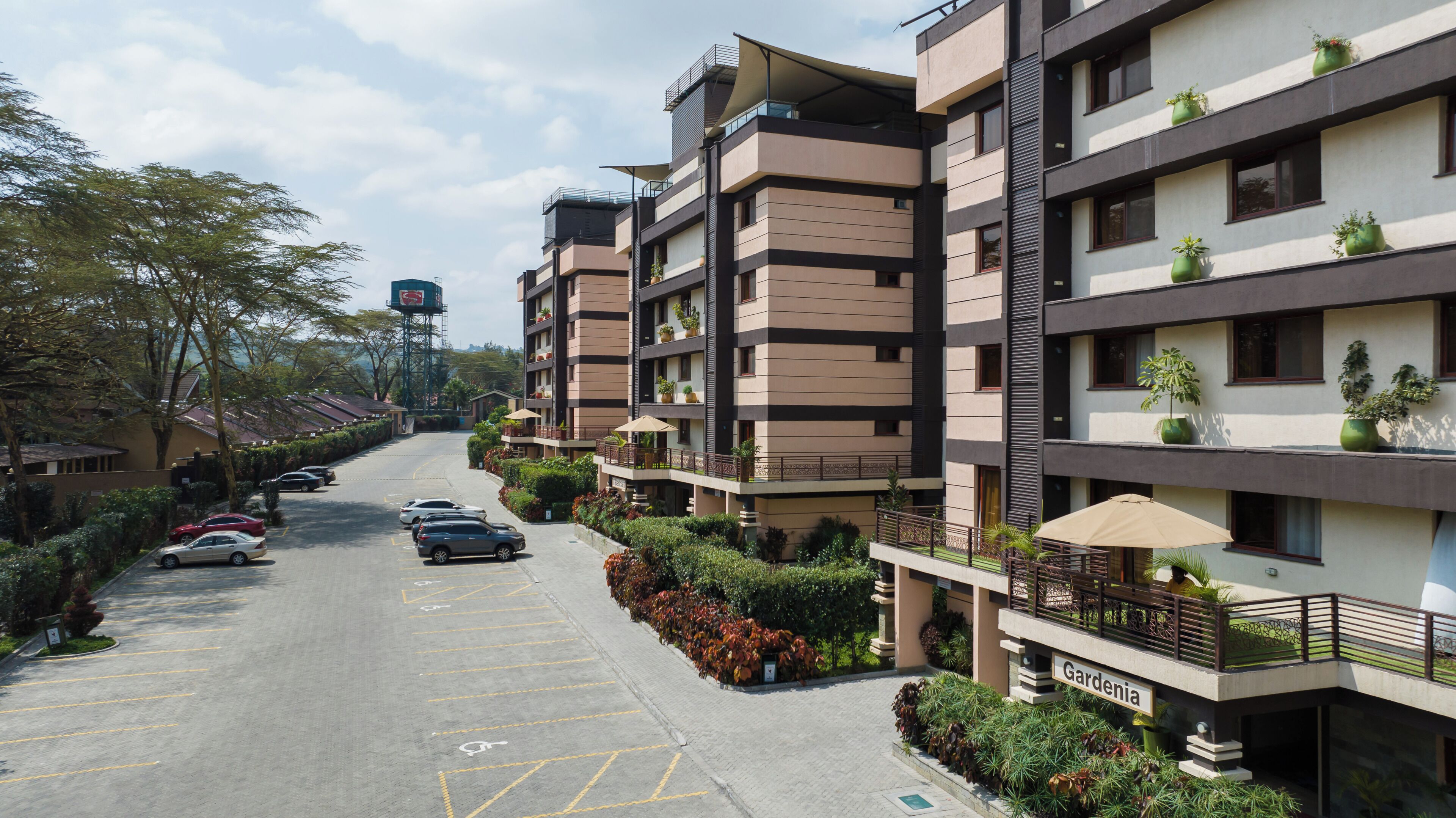 Un edificio residencial de varios pisos con balcones, un estacionamiento y un cartel que dice 'Gardenia'.