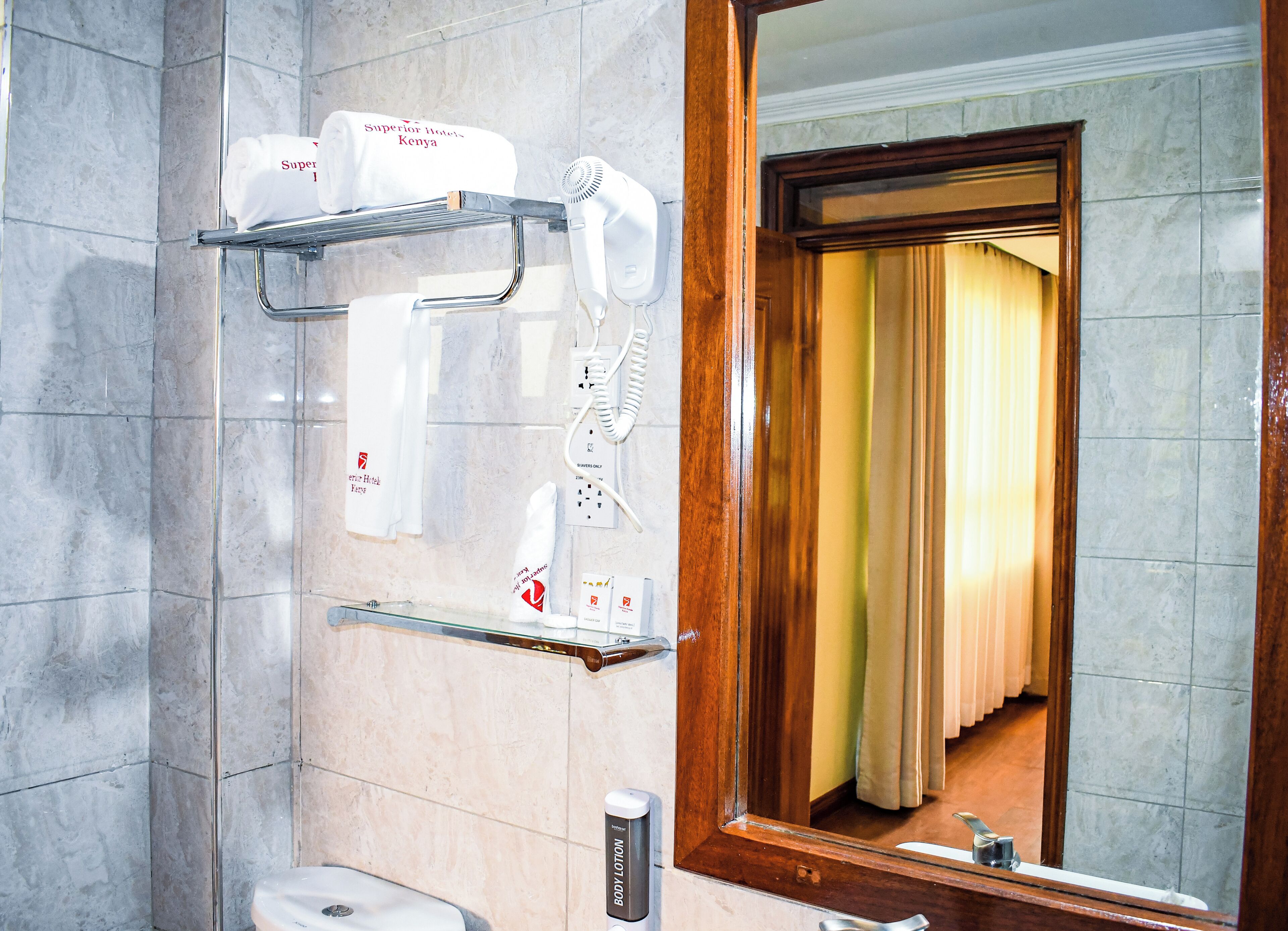 Un baño con espejo, perchero con toallas, secador de pelo, dispensador de jabón y cortina de ducha.