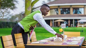 A person setting up a table outdoors with a number sign, a flower, and various dining items. - Lake Naivasha Resort (Naivasha)