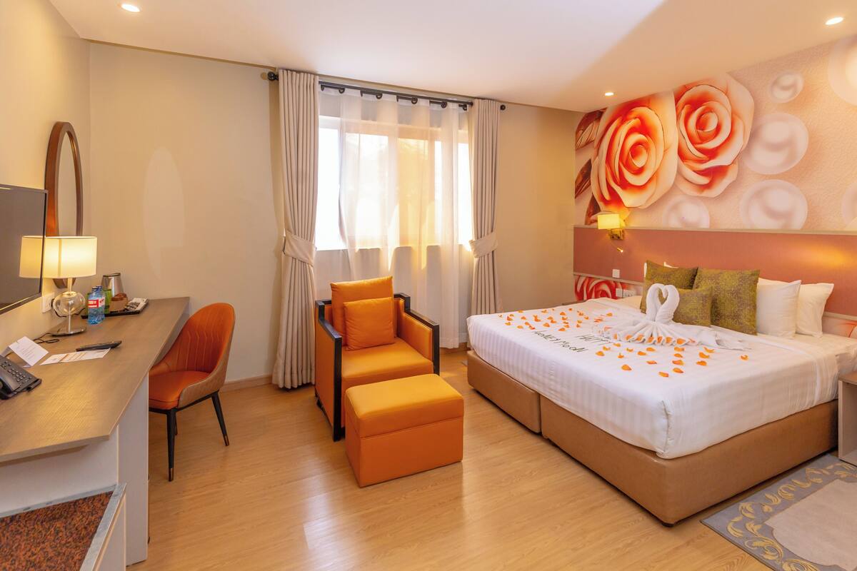 A hotel room with a bed, a desk, a chair, and a large window with curtains.