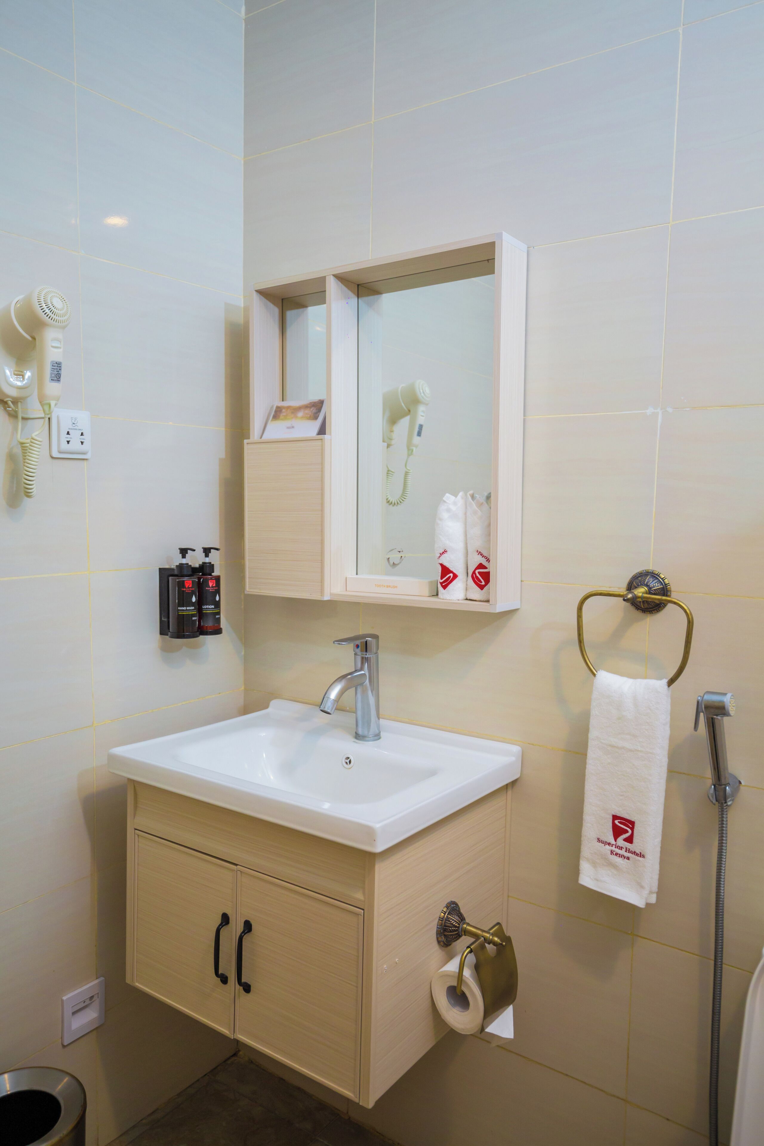 Un baño con lavamanos, espejo, toallero y dispensador de papel higiénico.