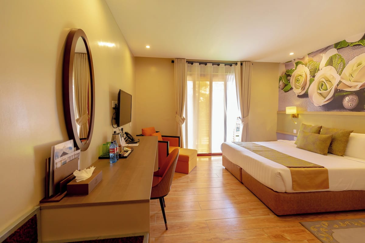 A hotel room with a bed, a desk with a chair, a television, and a large mirror.