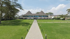 A building with a central walkway leading to a large entrance, surrounded by well-maintained lawns and trees. - Lake Naivasha Resort (Naivasha)