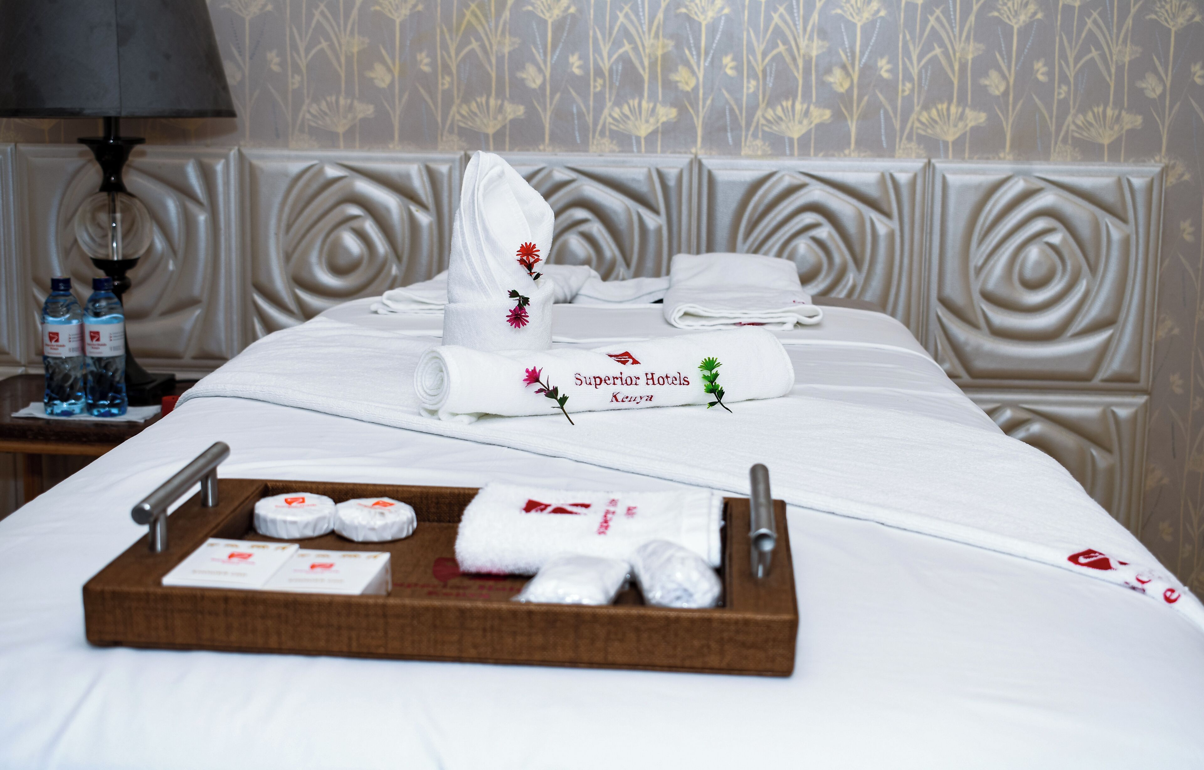 A hotel room with a neatly made bed, a tray with toiletries, and a decorative headboard.