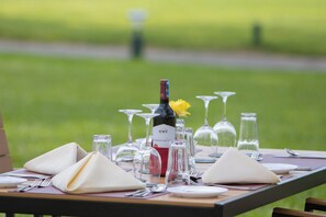 Une table dressée à l’extérieur, avec des verres à vin, une bouteille de vin et une fleur jaune.