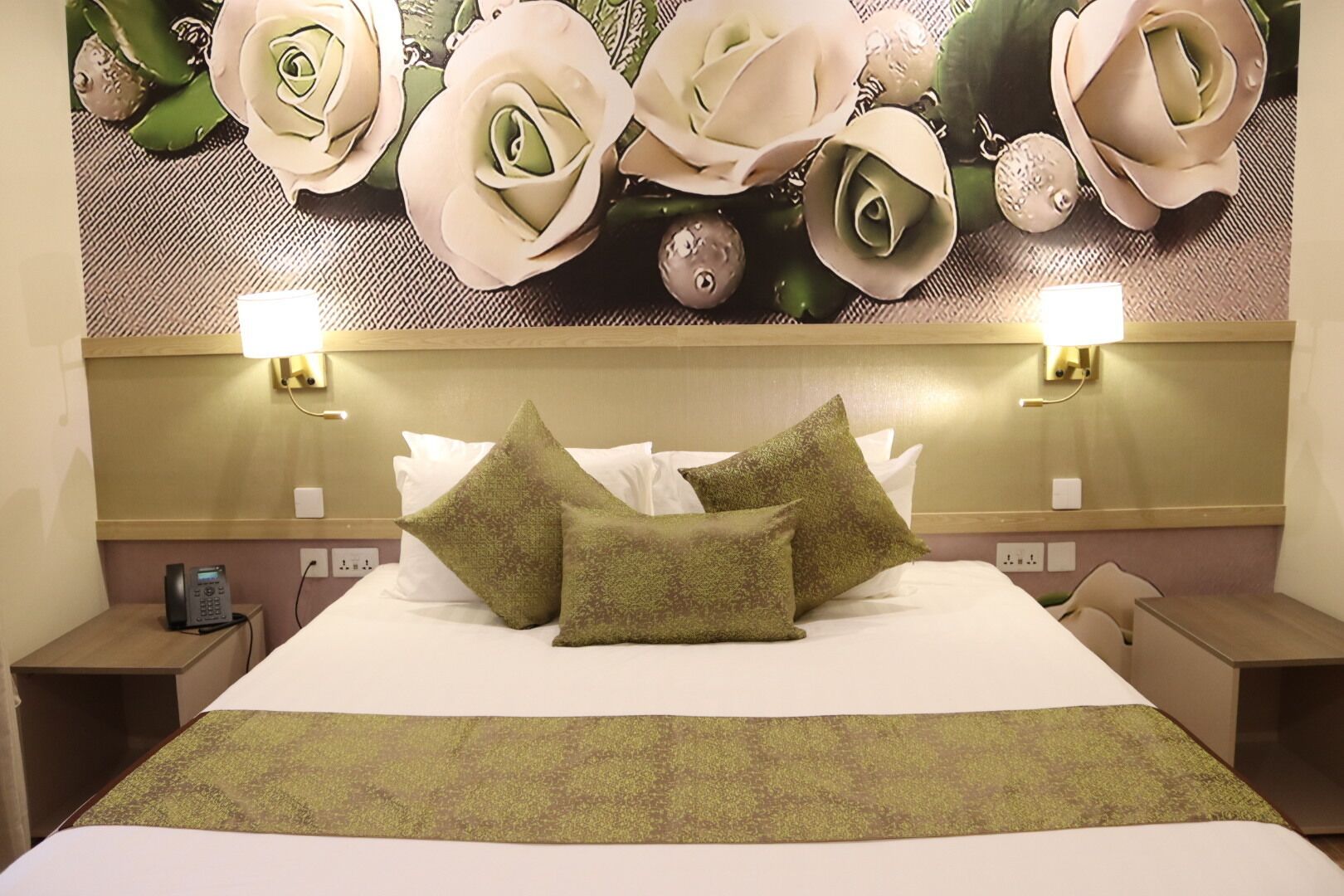 Una habitación de hotel con una cama grande, dos mesitas de noche, un teléfono y una pared con un mural floral.
