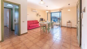 Amplia sala de estar con un sofá rojo, una mesa de comedor con sillas y una cocina visible a través de un arco.