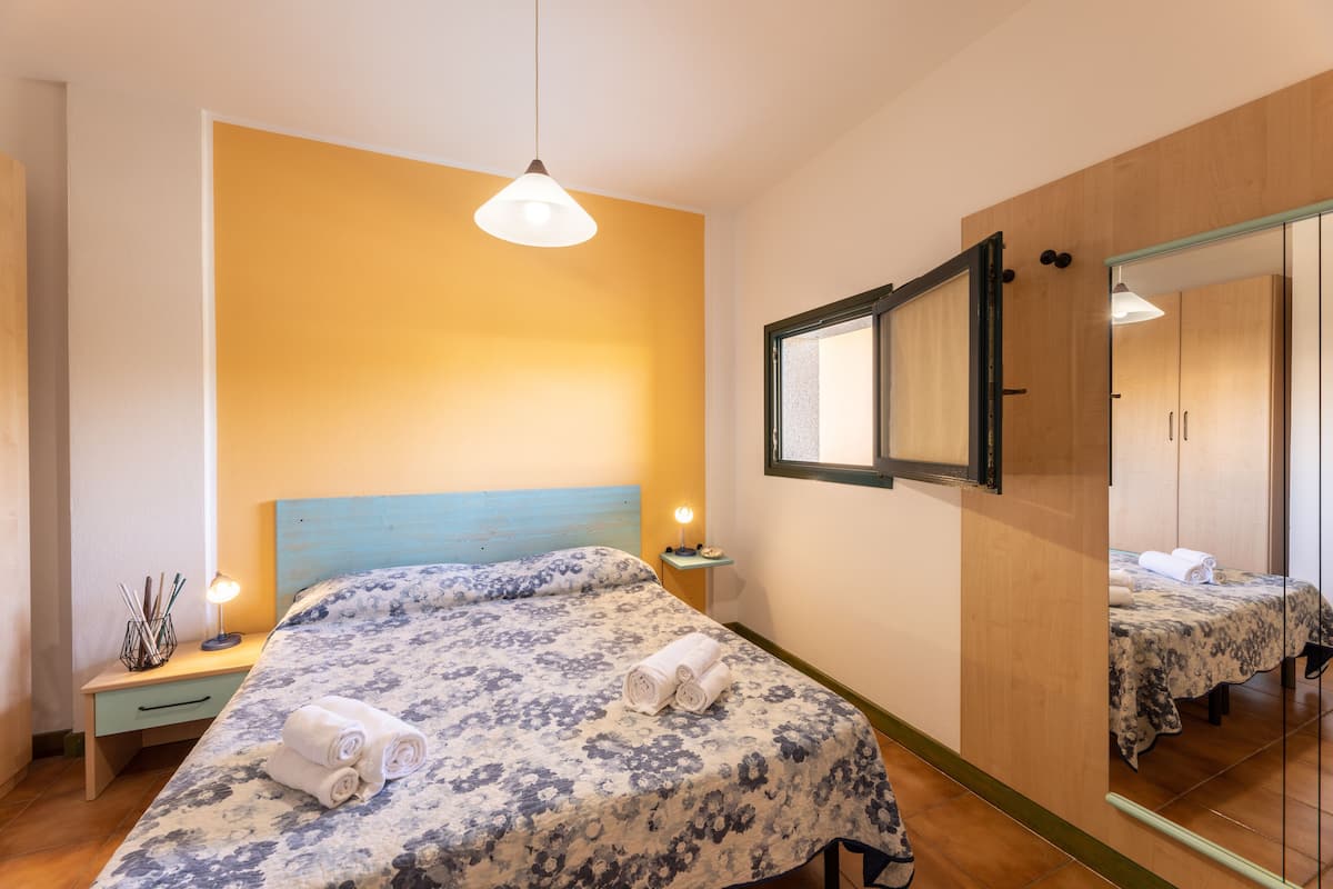A bedroom with a bed, bedside table, lamp, and a mirror.