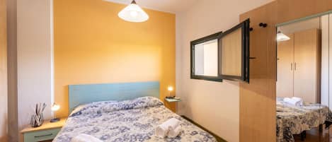 A bedroom with a bed, bedside table, lamp, and a mirror.