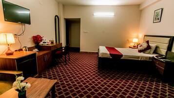 Ein Hotelzimmer mit Bett, Nachttisch, Lampe, Fernseher, Schreibtisch, Stuhl und einem gemusterten Teppich.