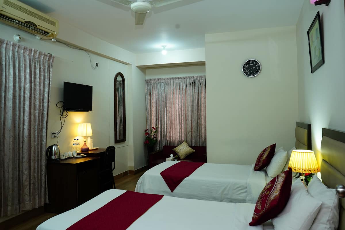 A hotel room with two beds, a desk with a lamp, a TV, and a clock on the wall.