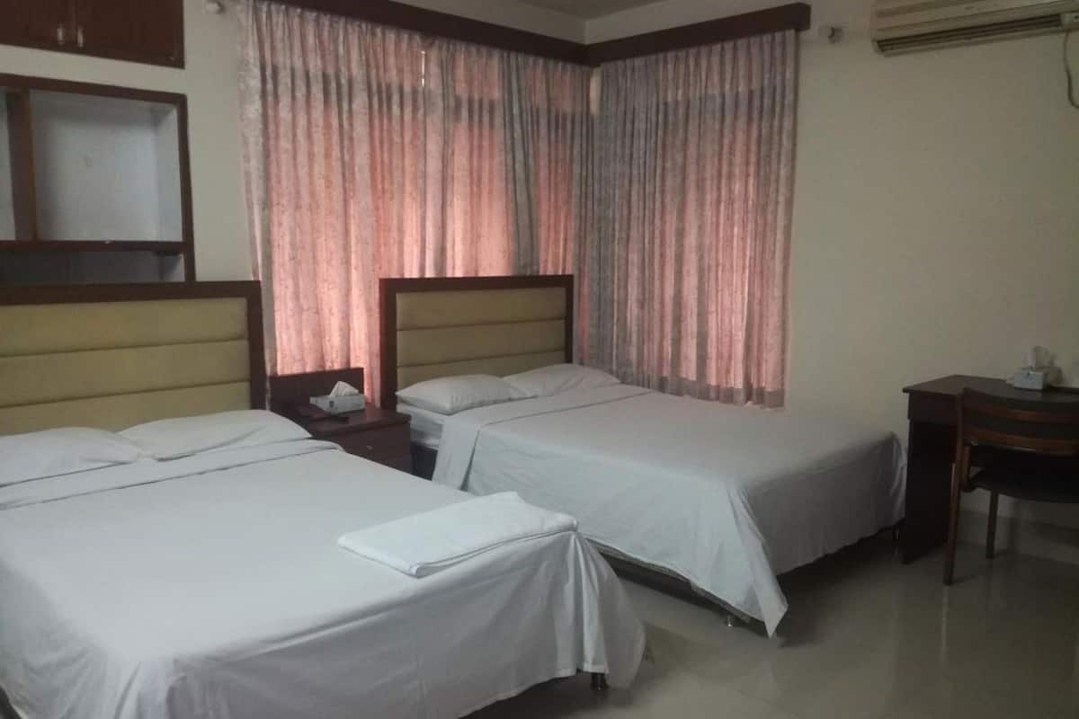A hotel room with two single beds, a wooden headboard, a nightstand with a lamp, and a desk with a chair.