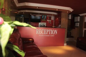 A reception area with a red counter, a television, and a framed portrait on the wall. - Bienvenue Delta Hotel (Nairobi)