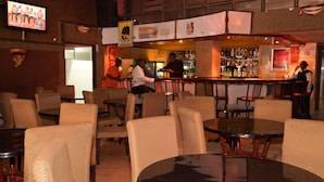 A bar area with round tables and chairs, a television screen, and a bar counter with bottles. - Bienvenue Delta Hotel (Nairobi)