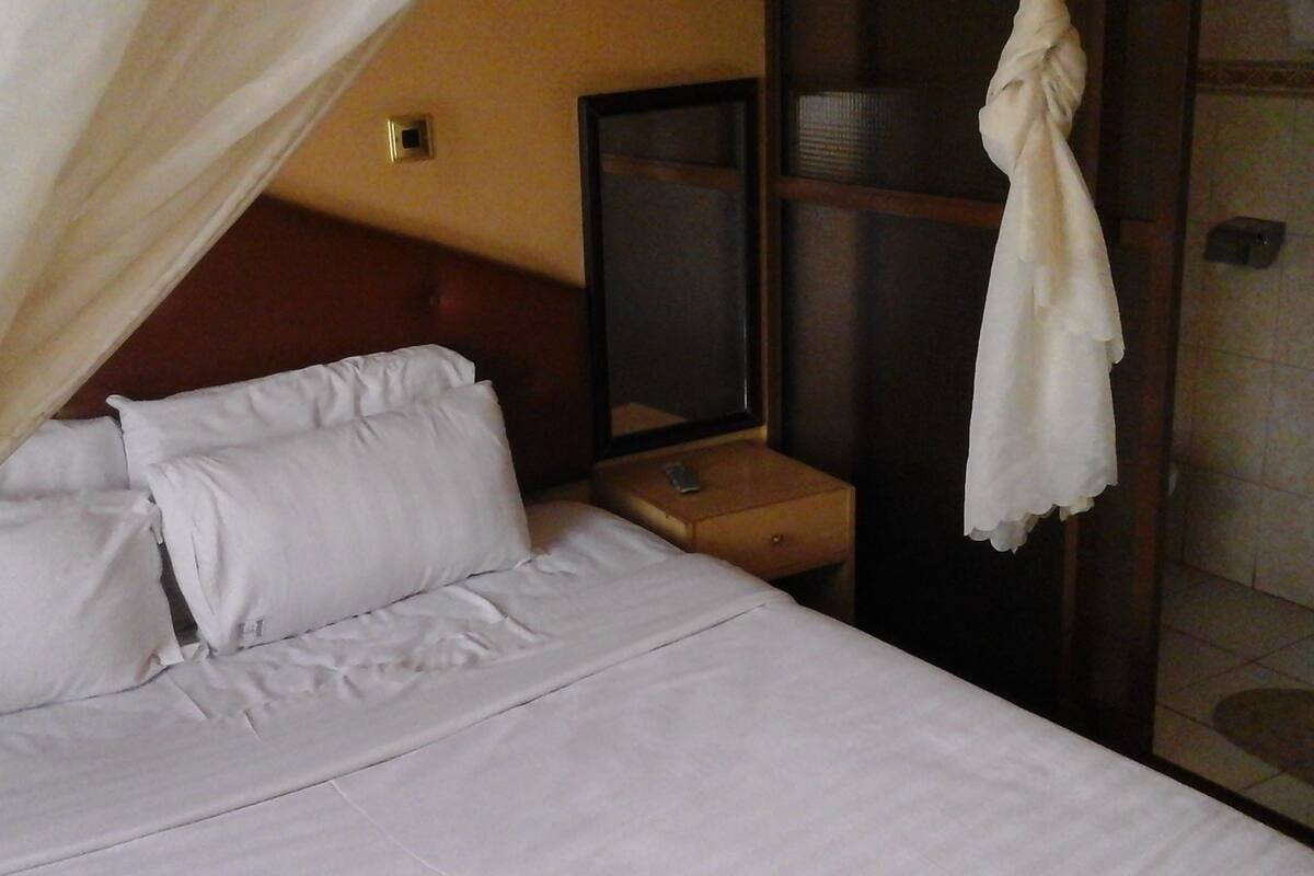 Una habitación de hotel con cama, mesita de noche, espejo y zona de ducha.