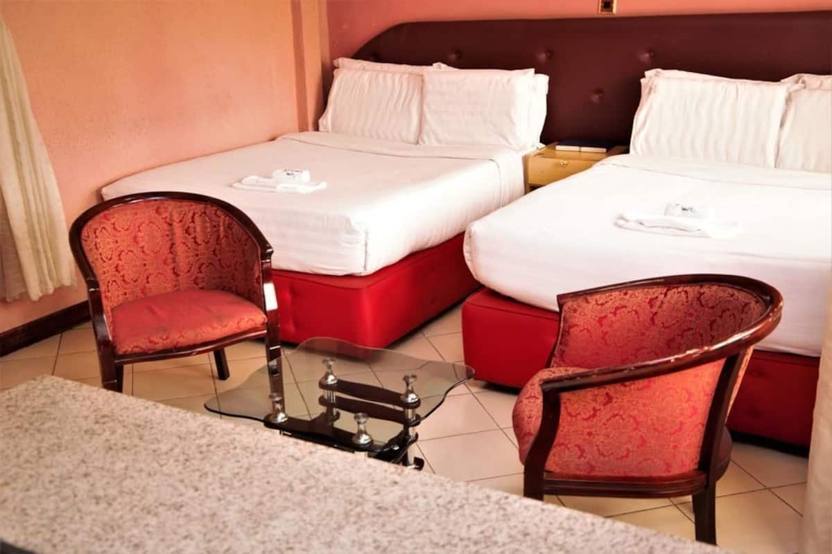 Una habitación de hotel con dos camas, una mesita pequeña y dos sillones.