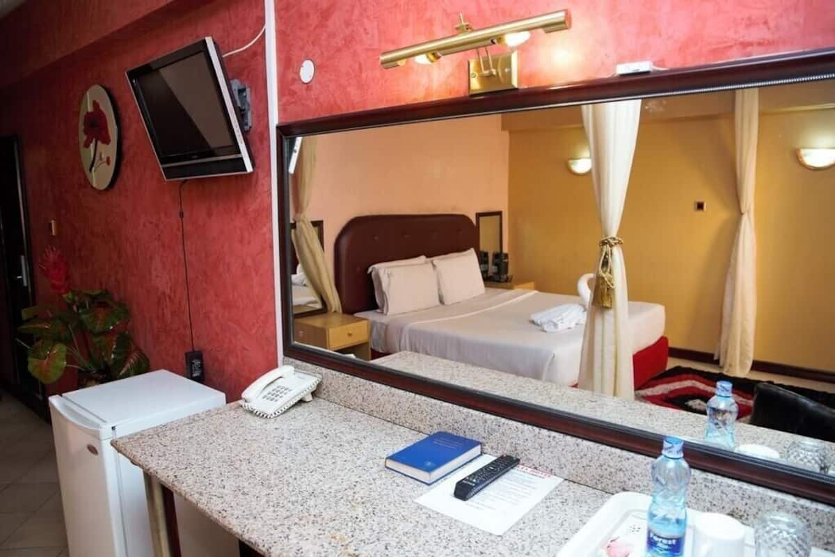 Una habitación de hotel con cama, mesita de noche, espejo y una pequeña kitchenette.