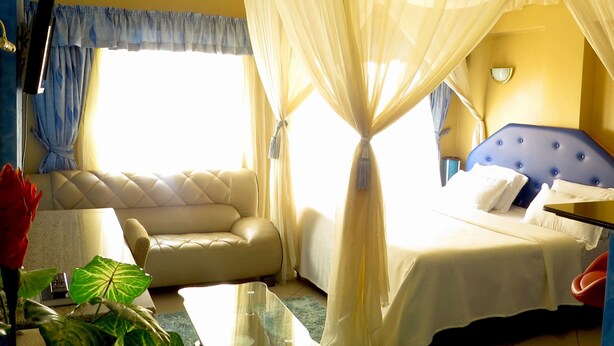 A hotel room with a bed, a sofa, a bedside table, and a window with curtains. - Bienvenue Delta Hotel (Nairobi)