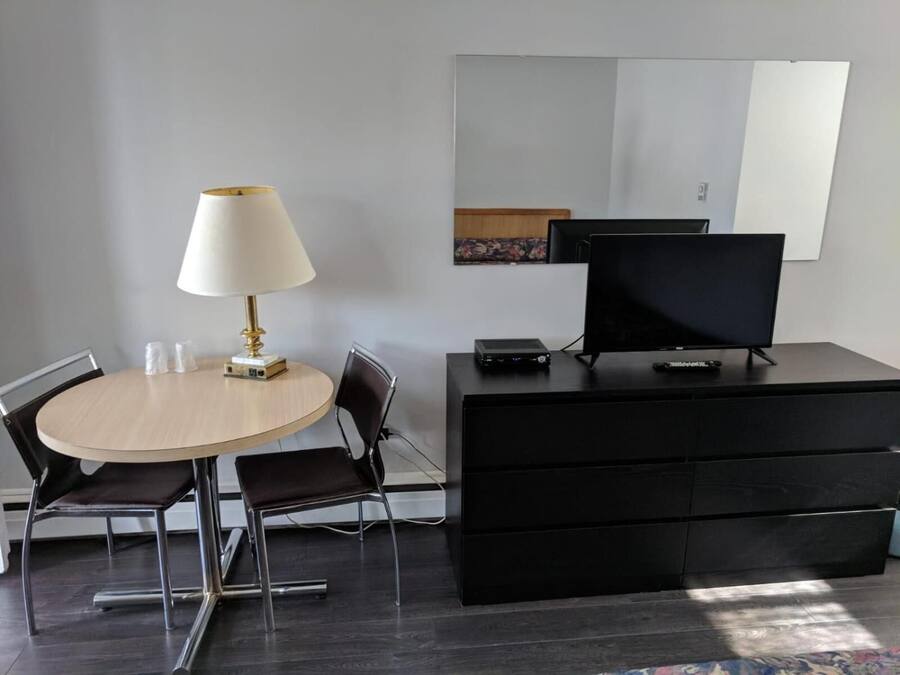 A modern room with a round table, two chairs, a lamp, a flat-screen TV, and a black dresser.