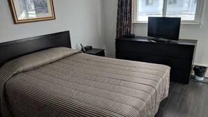 A hotel room with a large bed, a dresser, a television, and a window with curtains. - Hilltop Motel (Kingston)