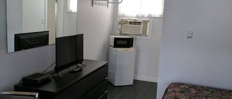 A room with a bed, a TV on a black dresser, a microwave, and a window with curtains.
