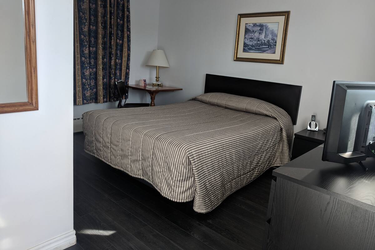 Habitación de hotel con una cama, un escritorio con lámpara, un cuadro en la pared y un televisor sobre un mueble.