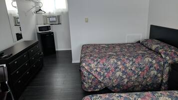 A bedroom with a bed, dresser, mirror, and a microwave.