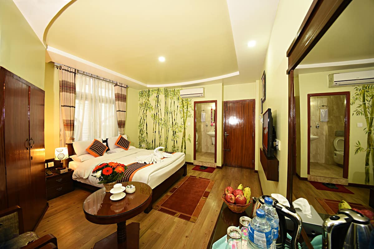 A hotel room with a bed, a dining table, a TV, and a bathroom visible through an open door.