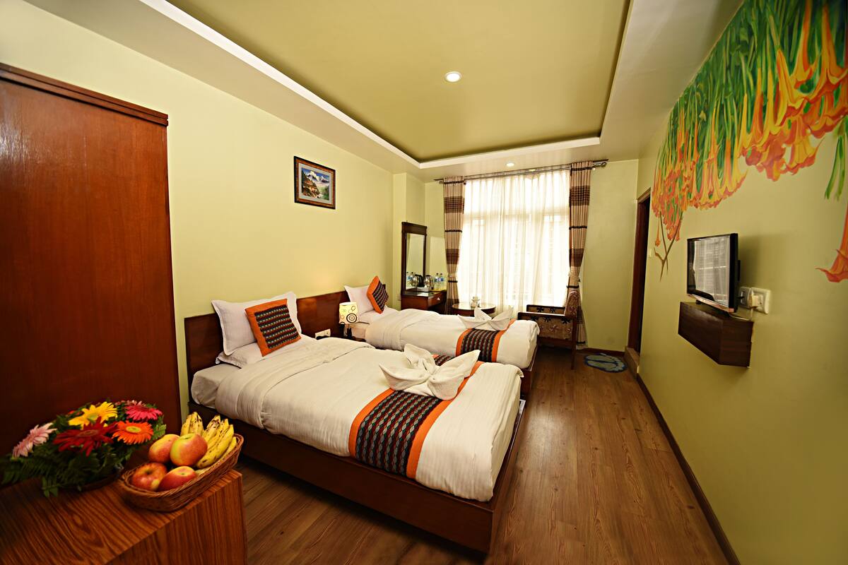 A hotel room with two beds, a wooden floor, a fruit basket, and a television on a shelf.