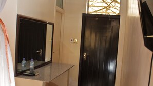 Um corredor estreito com uma porta de madeira, um pequeno balcão com um espelho e uma janela com grade de madeira.