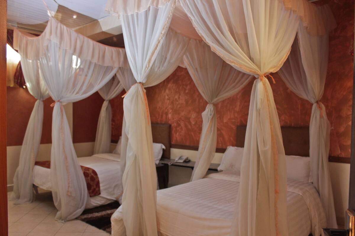 A hotel room with four beds, each with a canopy.