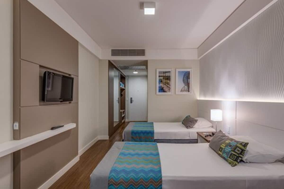 Ein Hotelzimmer mit zwei Betten, einem Fernseher und einem kleinen Schreibtisch mit einer Lampe.