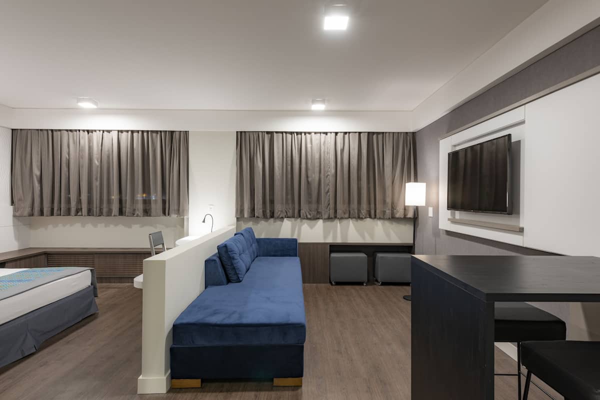 Ein modernes Hotelzimmer mit einer Couch, einem Schreibtisch, einem Fernseher und Vorhängen.