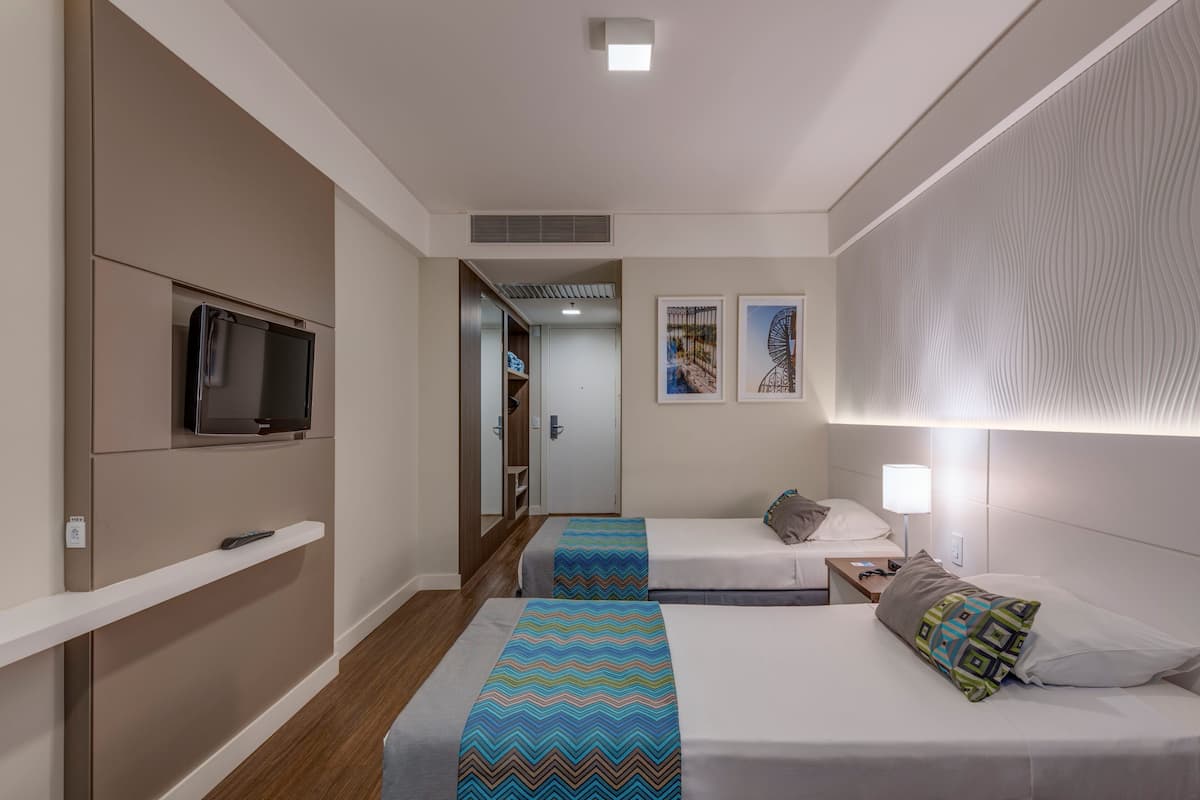 Ein Hotelzimmer mit zwei Betten, einem Fernseher, einem Nachttisch und einer Tür zu einem Badezimmer.
