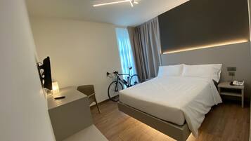 Una habitación de hotel moderna con cama, mesita de noche, lámpara, bicicleta y televisor montado en la pared.