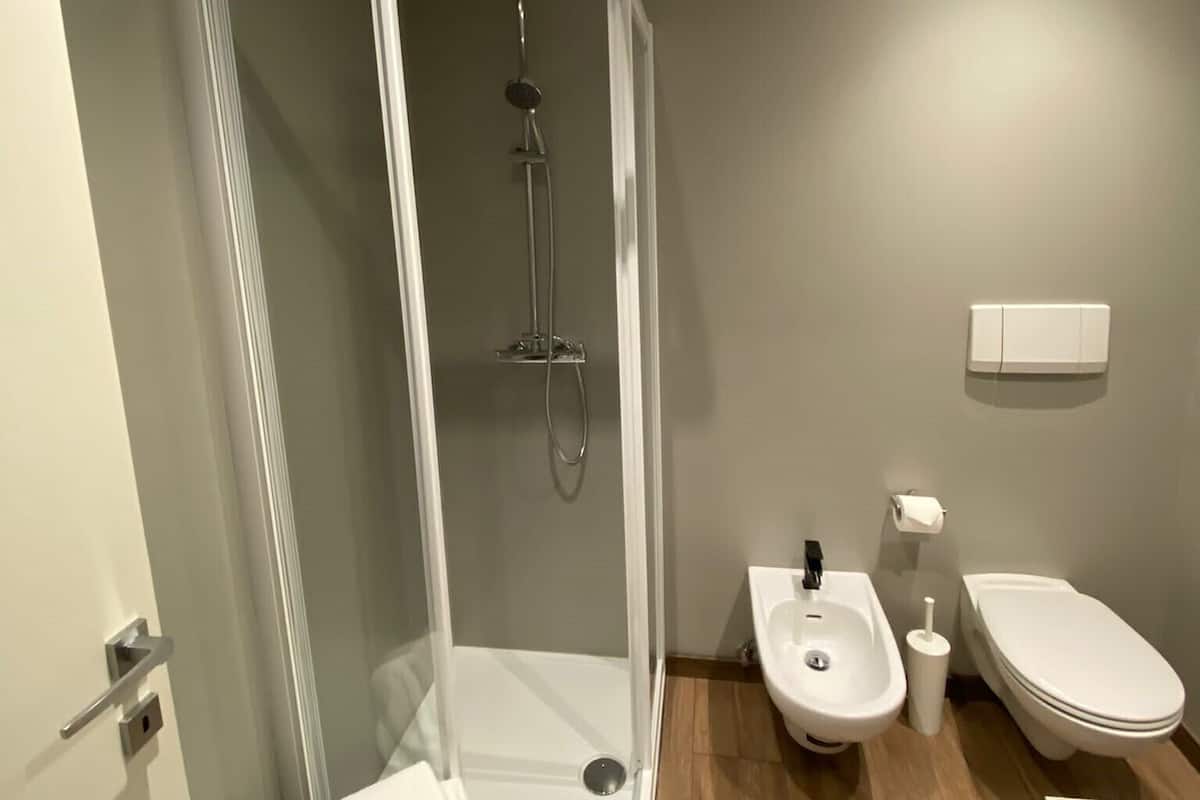 A modern bathroom with a glass-enclosed shower, a sink, a toilet, and a bidet.