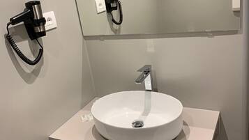Ein modernes Badezimmer mit einem runden weißen Waschbecken, einem Spiegel darüber und einem an der Wand montierten Föhn.