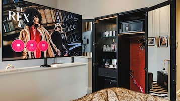 A room with a large flat-screen TV mounted on the wall displaying a movie poster. There is a black entertainment unit with shelves and a red carpeted area.