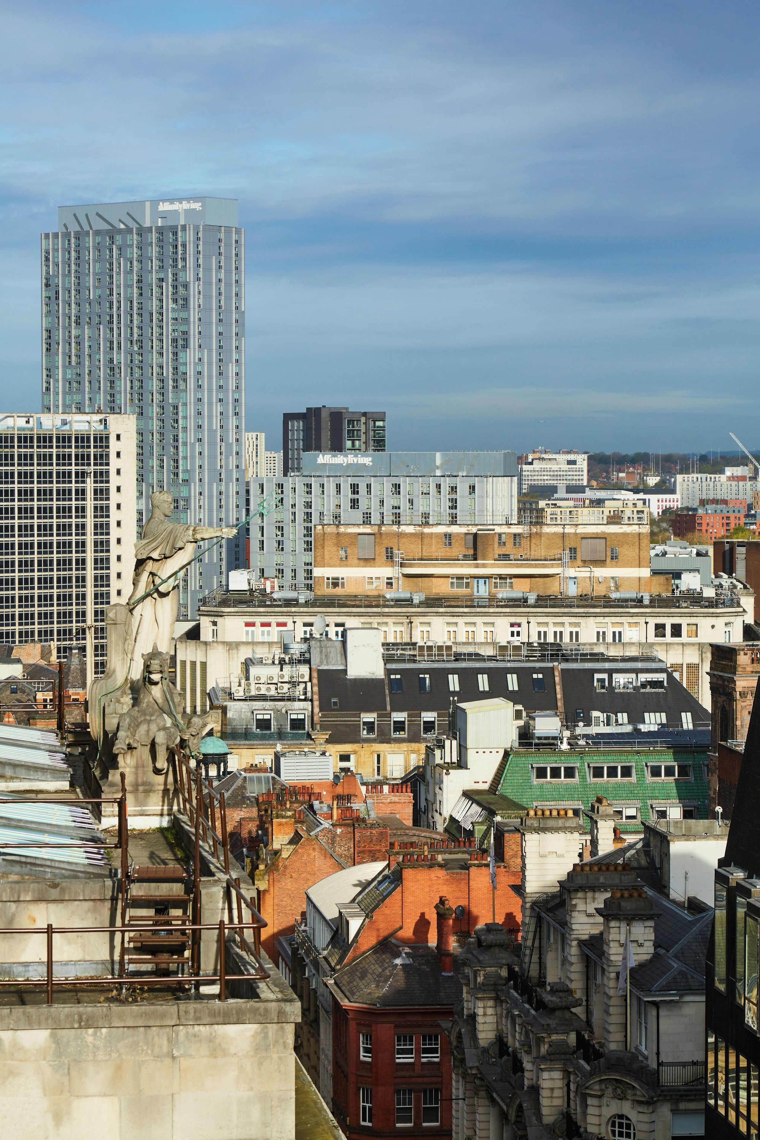 A cityscape with various buildings, including a tall modern structure and a statue on a rooftop.