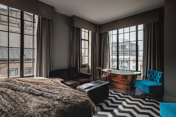 Una habitación con ventanas amplias, una bañera, un sofá y una silla.