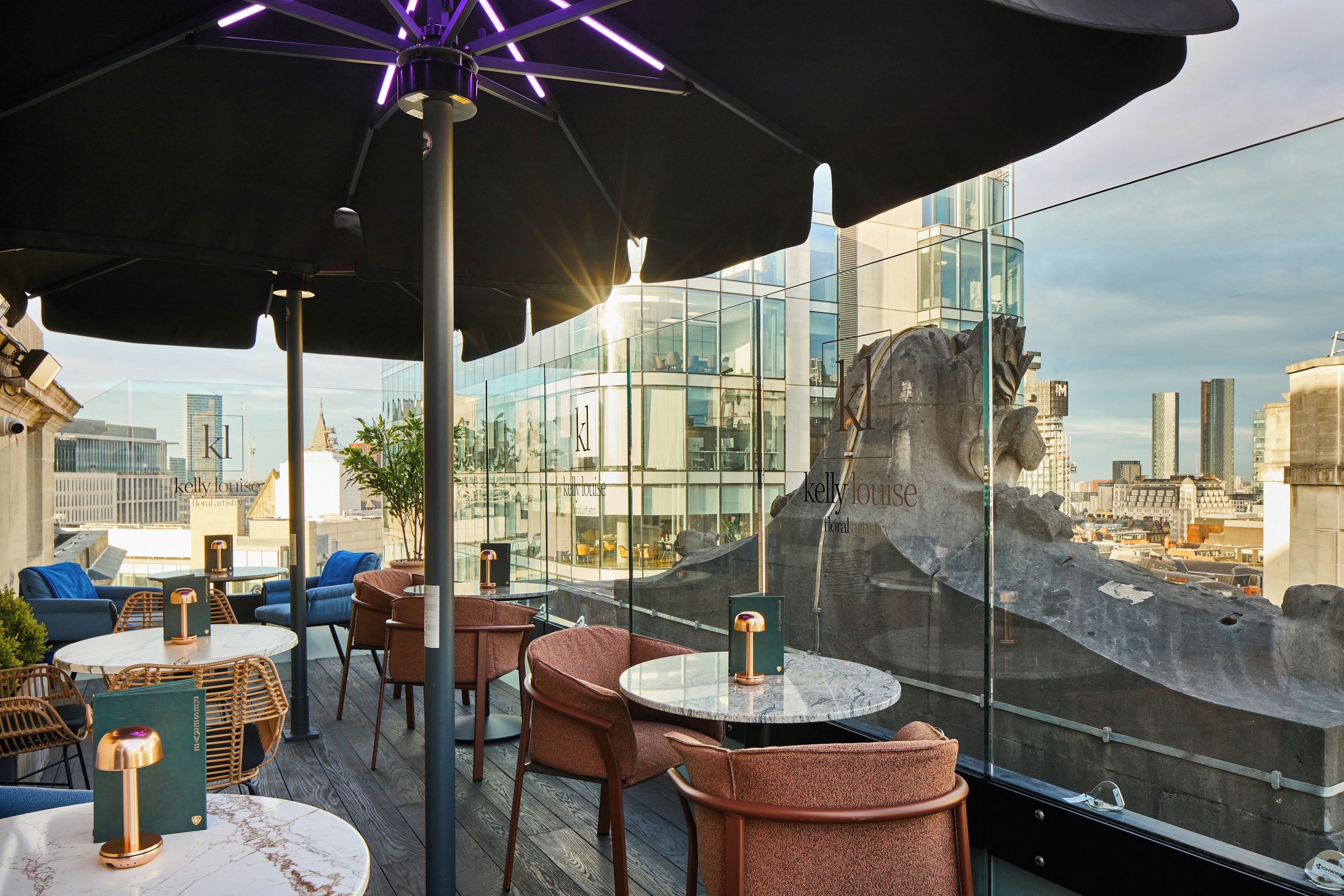 An outdoor seating area with tables and chairs, overlooking a cityscape with modern buildings.