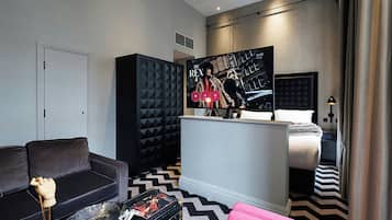 A modern hotel room with a sofa, a coffee table, a TV, a bed, and a patterned floor.