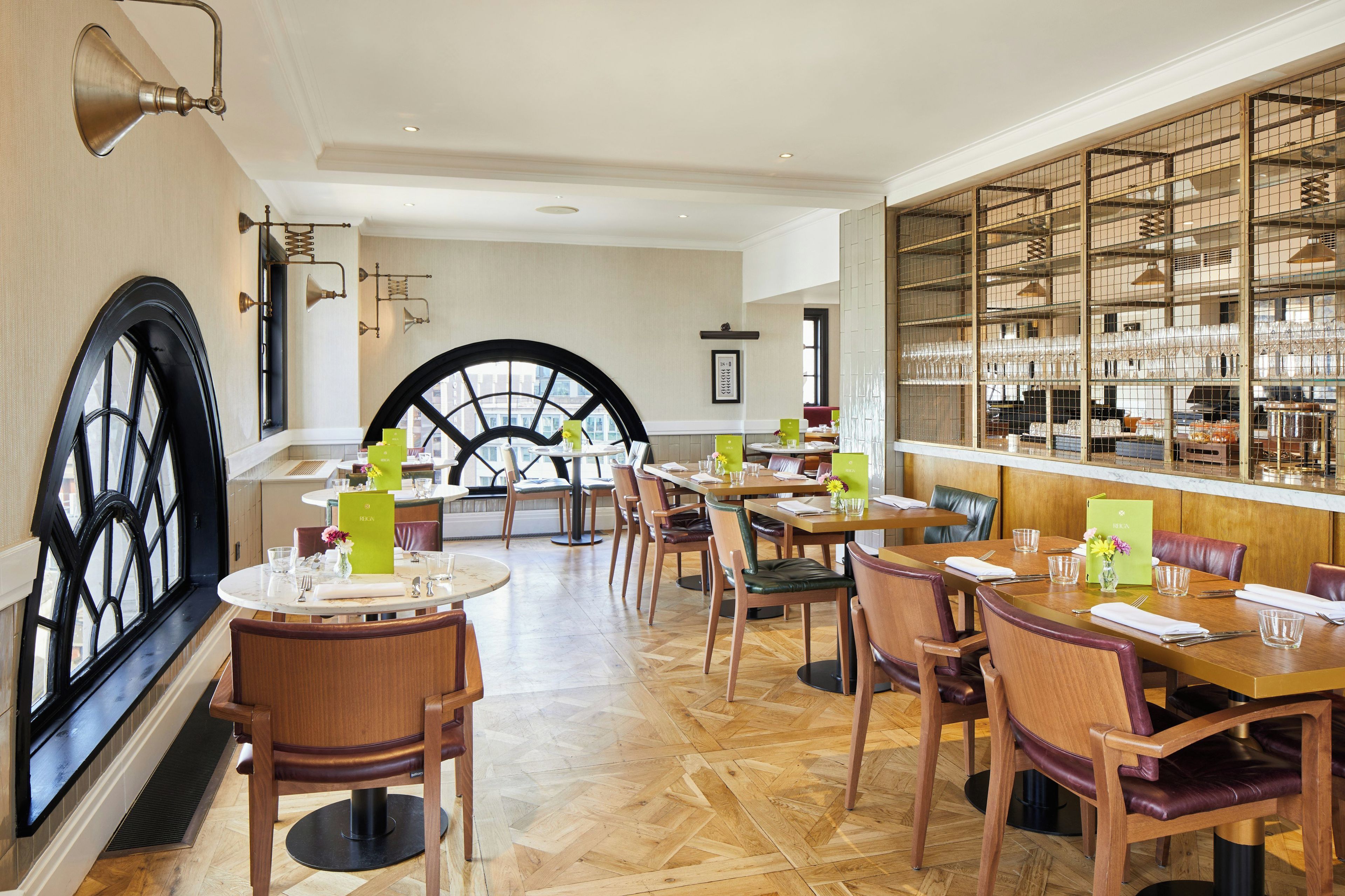 Un restaurant doté de nombreuses tables et chaises, d’une grande fenêtre en arc de cercle et d’un mur orné d’un motif en réseau.