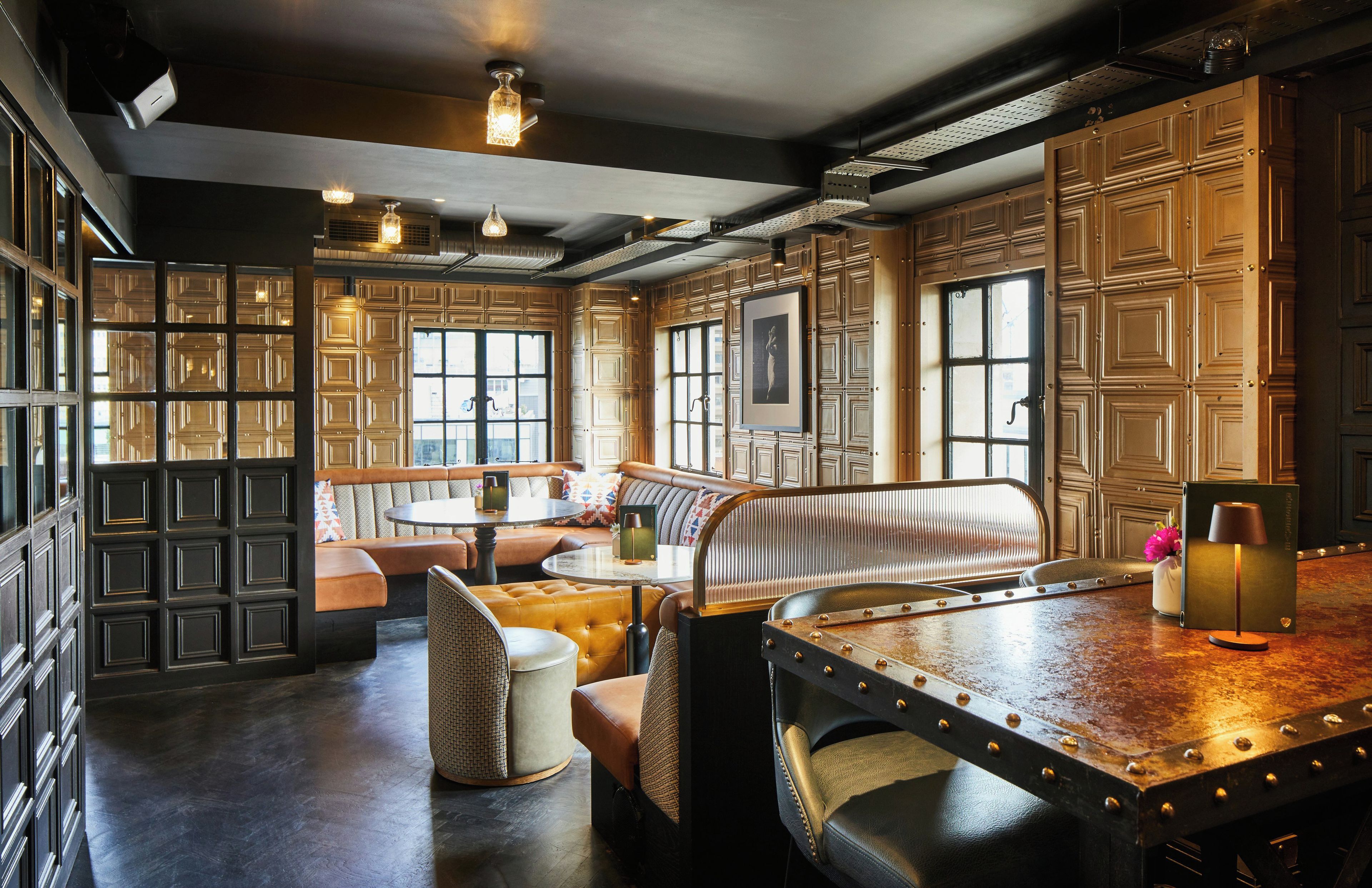 A room with a wooden bench, a table, and a sofa. There are multiple windows and a door.