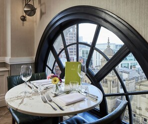 Mesa para dos personas con vistas a un paisaje urbano a través de un ventanal grande.