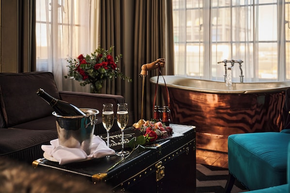 Ein Zimmer mit schwarzem Koffer, Champagner, Gläsern, einem Blumenstrauß und einer Badewanne.