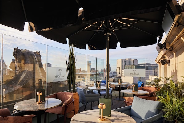 A rooftop terrace with outdoor seating, city views, and a statue. - The Rex – Formerly Hotel Gotham (Manchester)