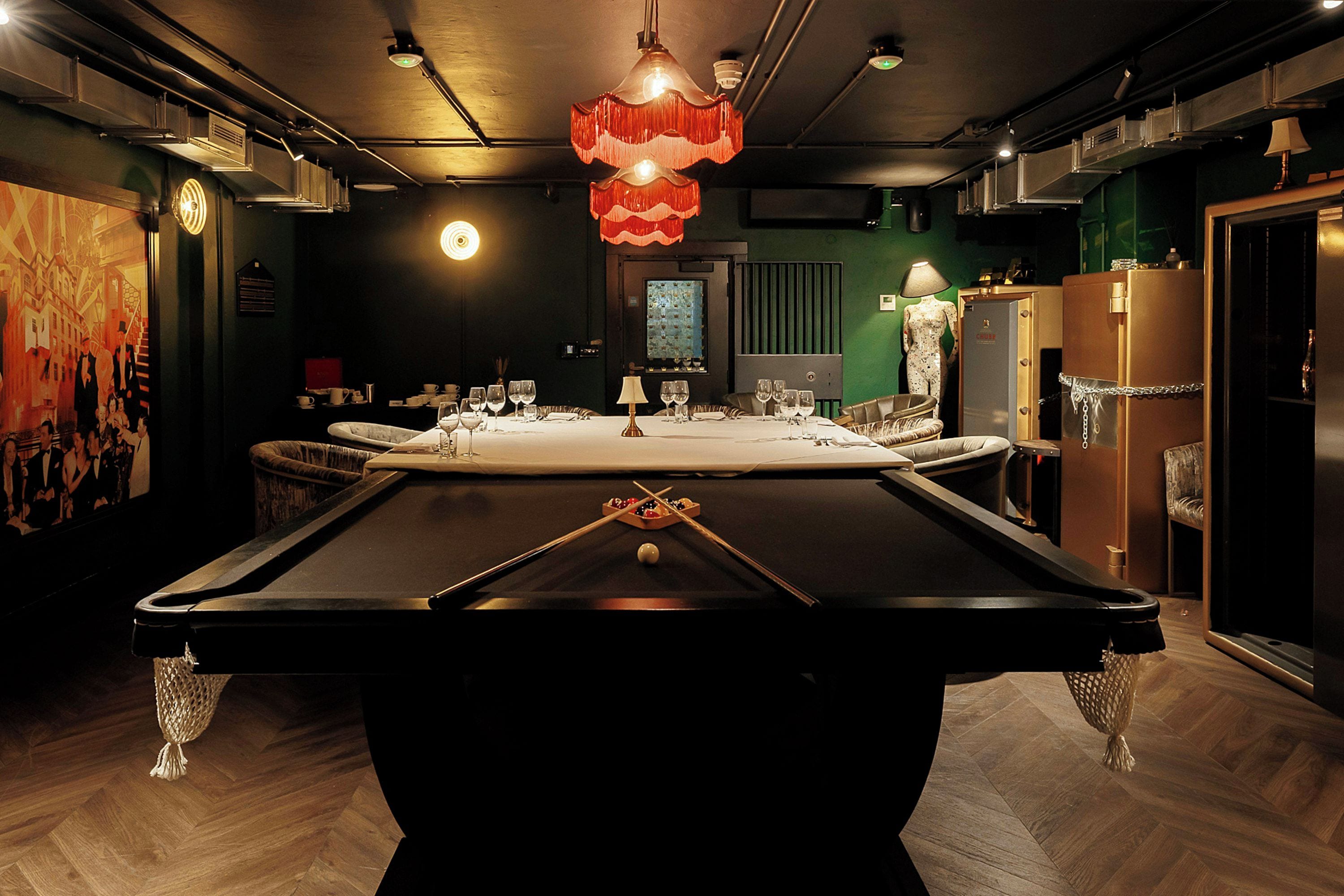 A pool table with a billiard cue in the foreground, surrounded by chairs and a table set for dining.
