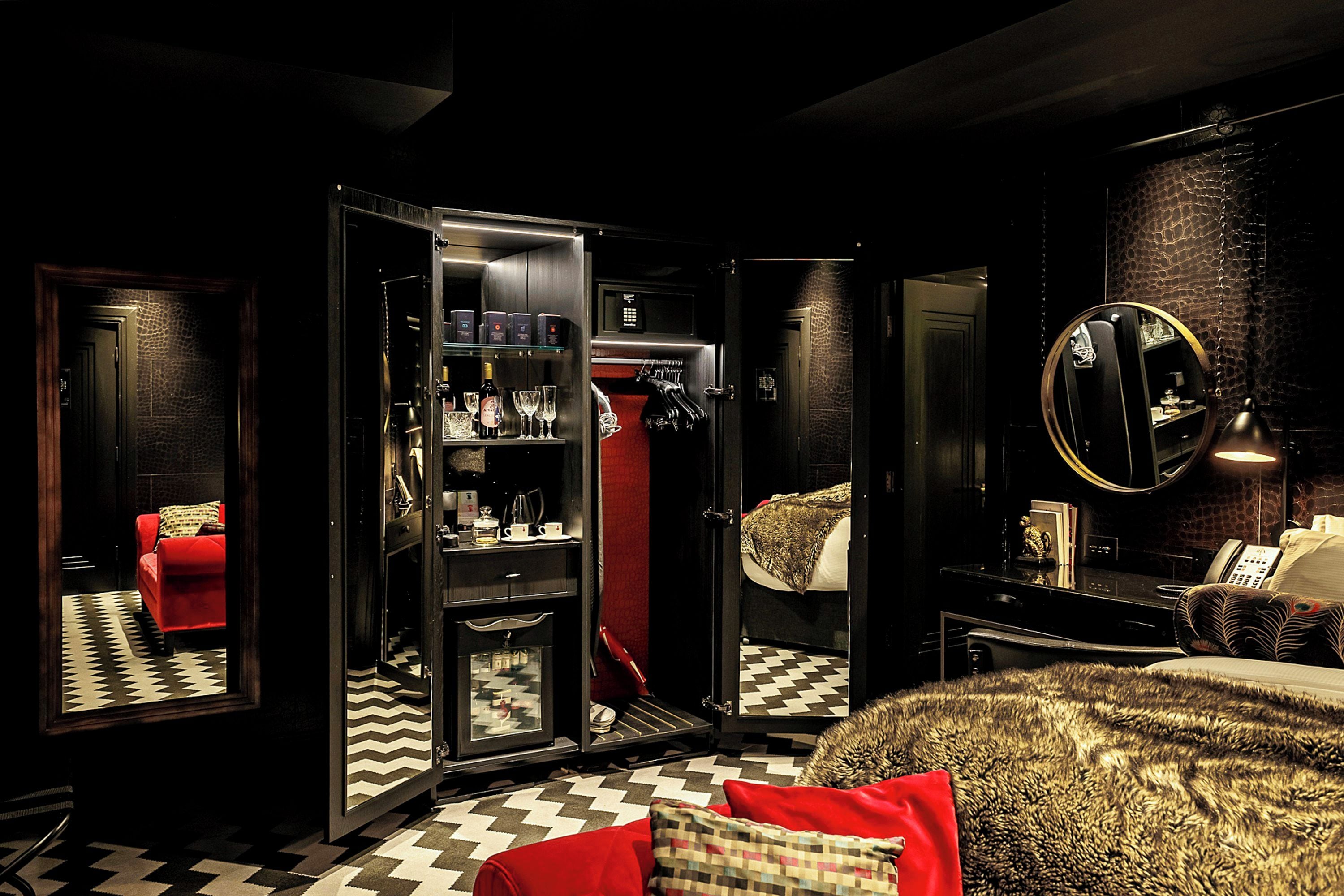 A hotel room with a checkered floor, a red sofa, a wardrobe with a mirror, and a bed with patterned bedding.
