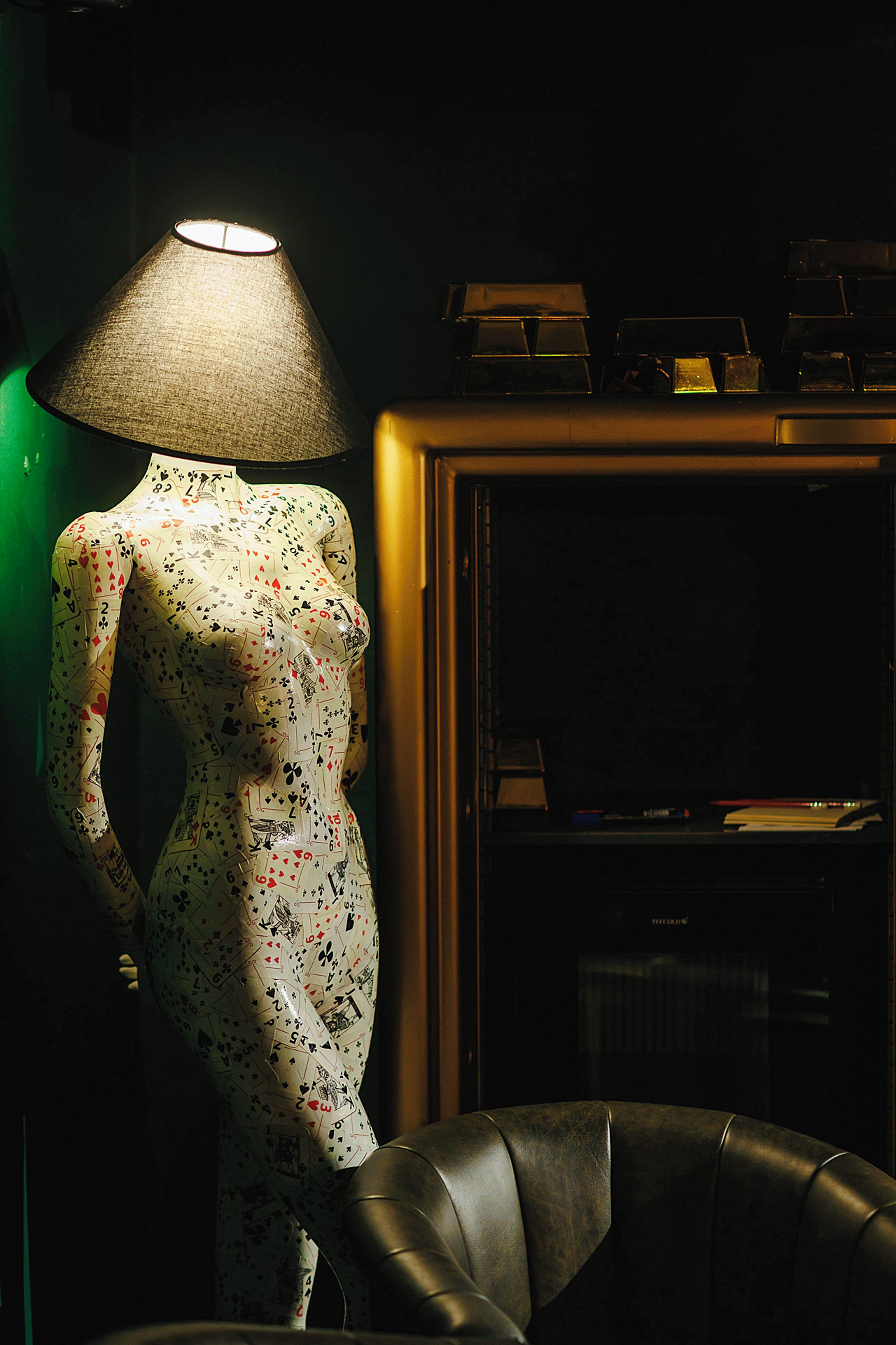 A mannequin in a patterned dress with a lamp and a cabinet in the background.
